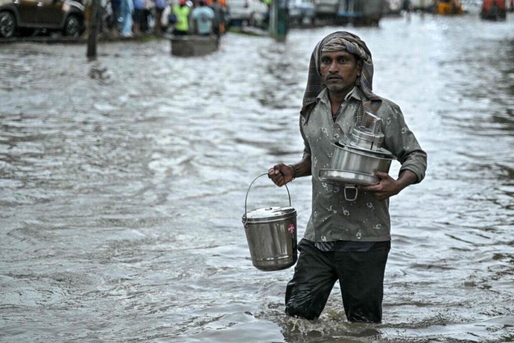 Mutfak eşyaları taşıyan bir adam, 22 Ekim 2024'te Bengaluru'da su basmış bir caddeden geçiyor